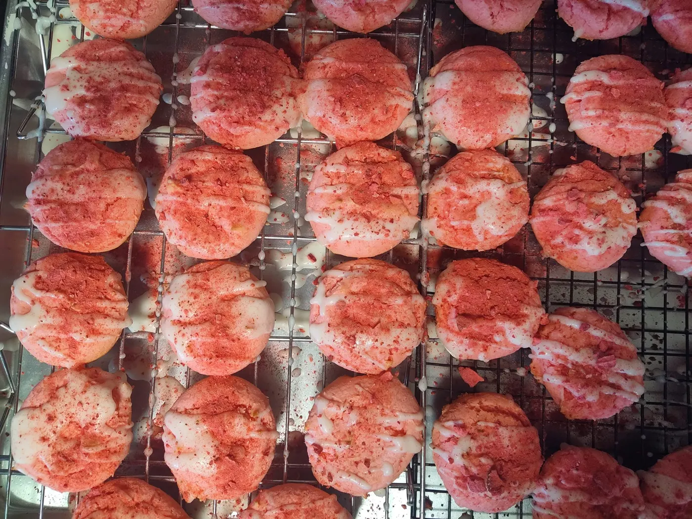 Strawberry crunch cookies with vanilla drizzle cooling on a wire rack at Horror Ghouls Bakery